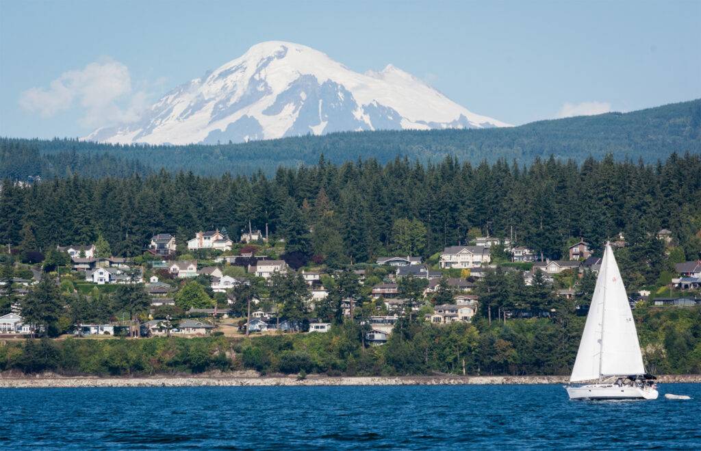 Sailboat on the water with a snow-capped mountain and forested shoreline in the background