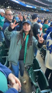 A fan in a cap holding up two peace signs among Mariners fans at BoatLaw's ALCS Game 3 outing